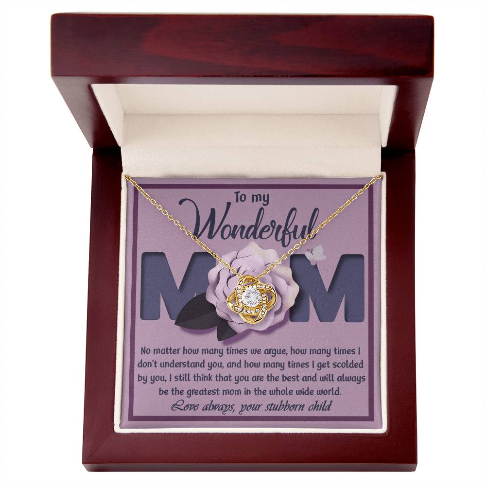 The "To Mom, The Greatest Mom - Love Knot Necklace" features a delicate flower-shaped pendant adorned with cubic zirconia crystals. It is beautifully packaged in a box with a heartfelt message expressing love and appreciation for mom, despite occasional disagreements, signed "Your stubborn child.