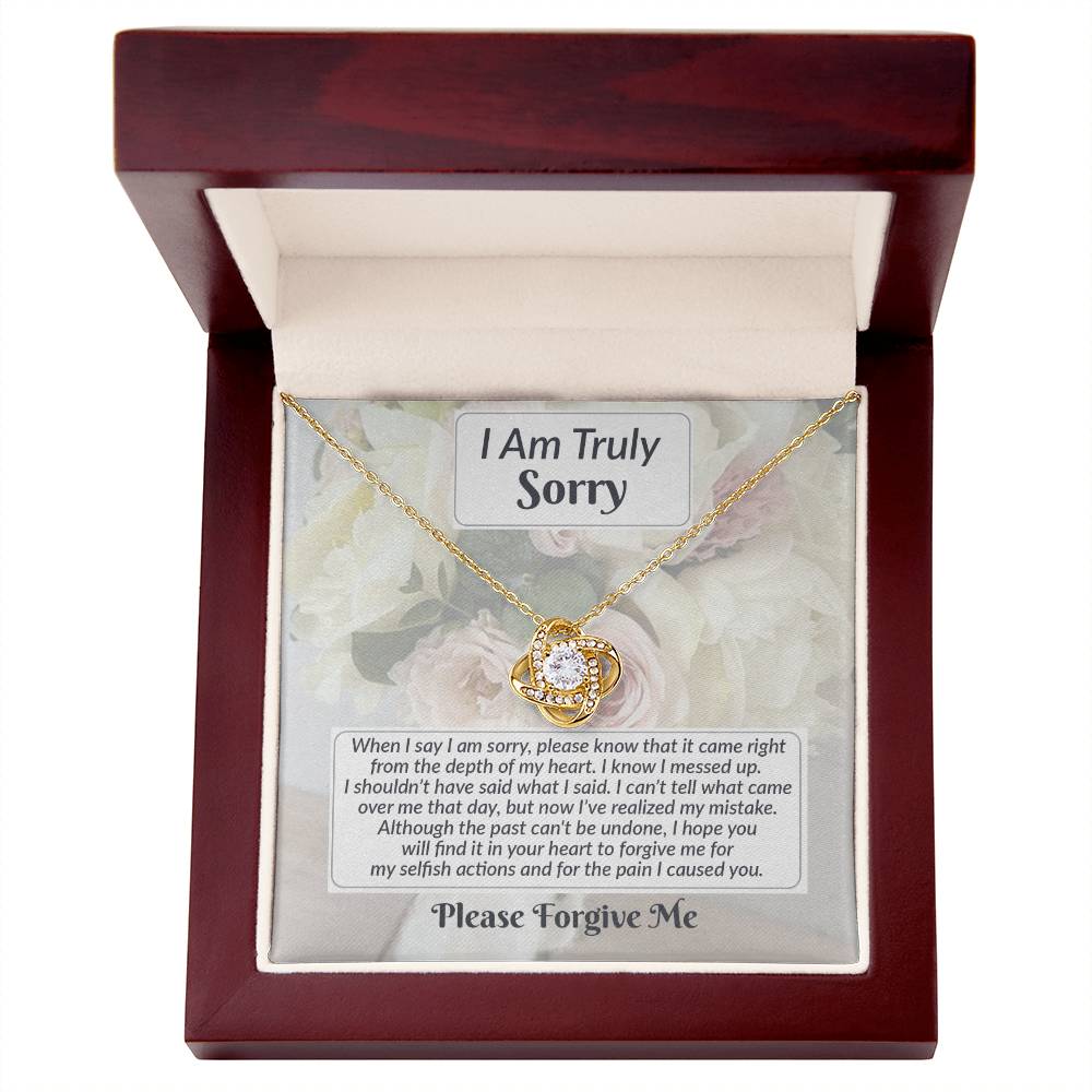 A Sorry-What I Said - Love Knot Necklace, featuring a diamond pendant, is showcased in an open wooden box adorned with cubic zirconia crystals and accompanied by a heartfelt apology message on the inner lid.