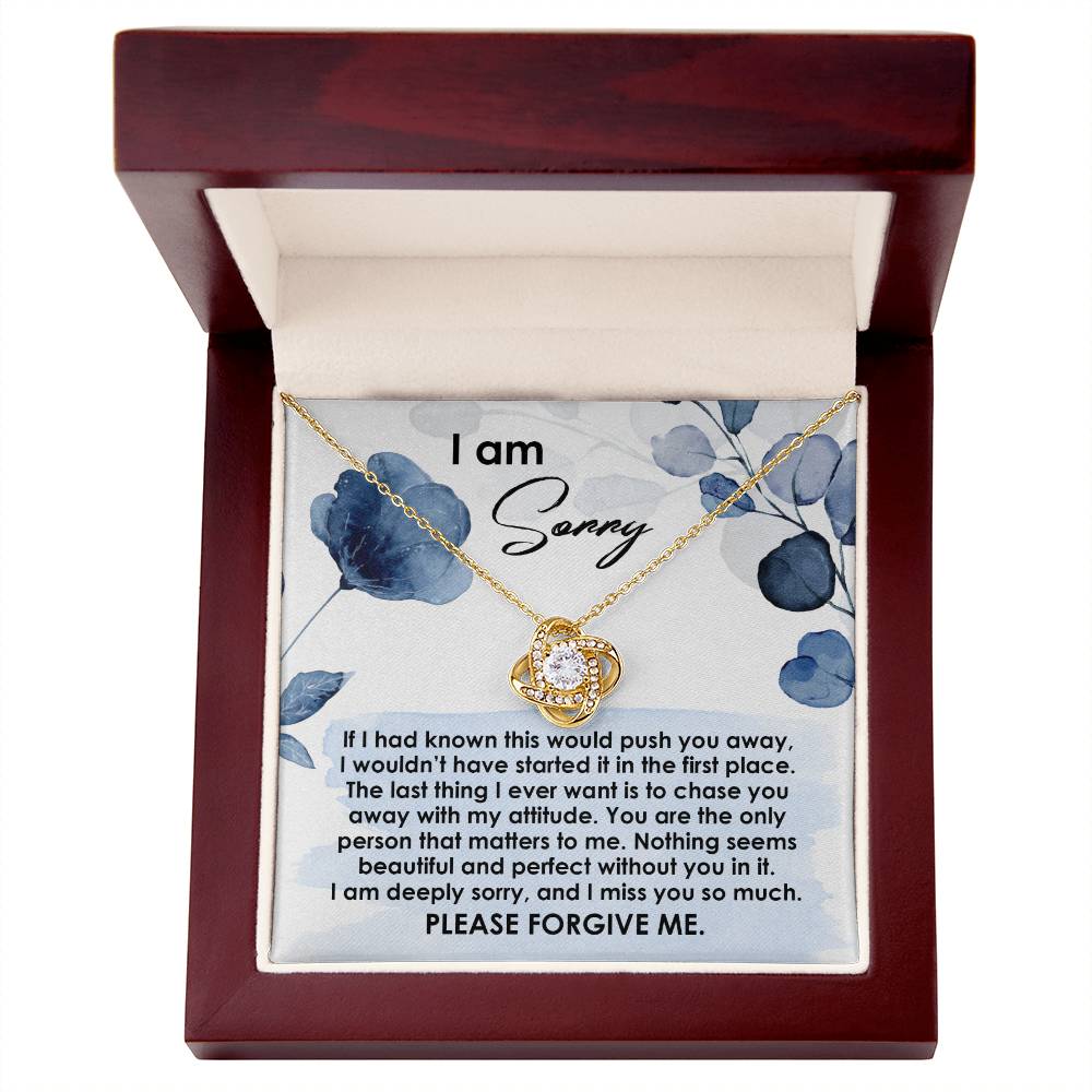 The Sorry-Push You Away - Love Knot Necklace comes with a round pendant adorned with cubic zirconia crystals in a gold finish, perfectly placed in a wooden box. The lid of the box reads "I am Sorry," and contains a heartfelt apology note inside.