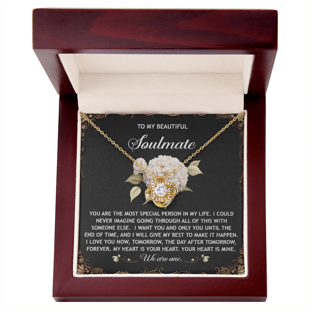 The Soulmate-We Are One Love Knot Necklace, adorned with cubic zirconia crystals, is nestled in a wooden box with a floral background and features a heartfelt message for your soulmate.