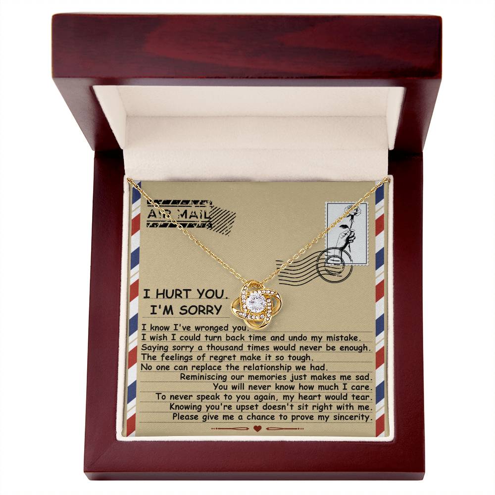 A Sorry-Makes Me Sad - Love Knot Necklace adorned with cubic zirconia crystals is presented in a wooden box. The inside of the lid features a letter containing an apology message and an "Air Mail" illustration, creating a truly personalized gift.