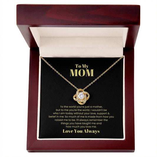 A "To My Mom, To The World You Are Just  A Mother - Love Knot Necklace" with a heart-shaped pendant, adorned with cubic zirconia, in a gift box featuring a message to a mother expressing love and gratitude.