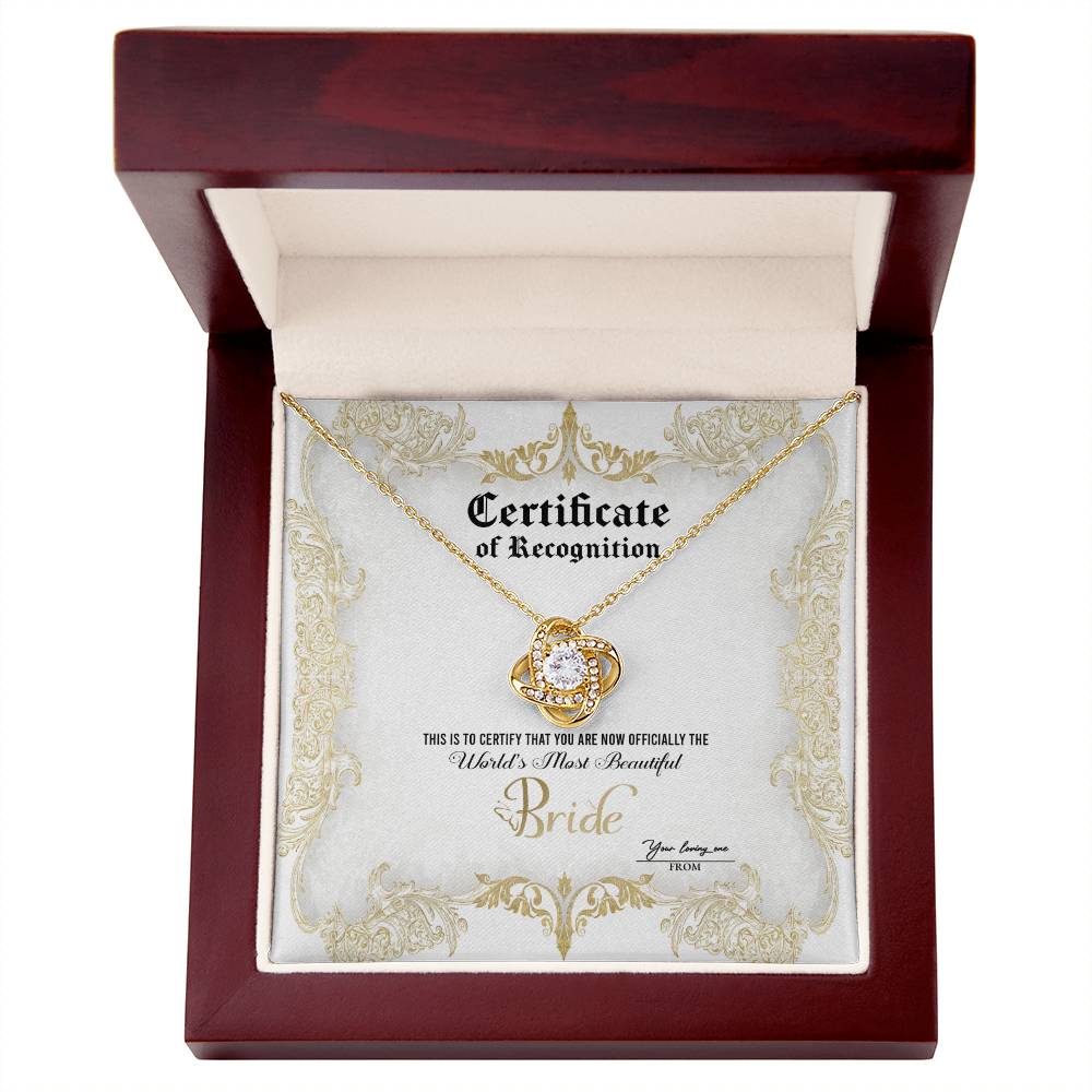 A To Bride, Certificate Of Achievement - Love Knot Necklace with a diamond-studded pendant is inside a box labeled "Certificate of Recognition" with text declaring "World's Most Beautiful Bride" and a space for names "You bring me" and "From." The pendant, set in 14k white gold, sparkles brilliantly.