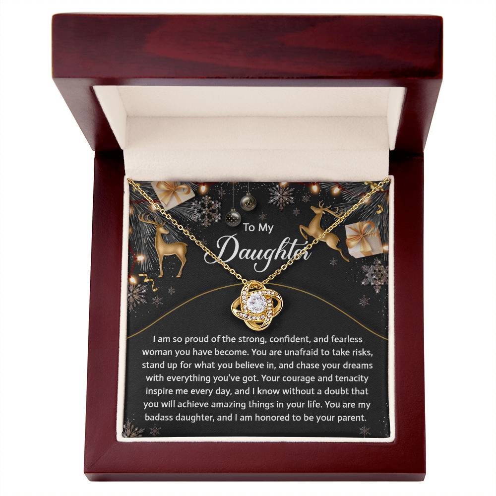 The Daughter-Amazing Things Love Knot Necklace, featuring a central stone elegantly surrounded by cubic zirconia crystals, is showcased in a red box. This personalized gift comes with a heartfelt message for your daughter, expressing pride and encouragement, set against a backdrop adorned with snowflakes and stars.