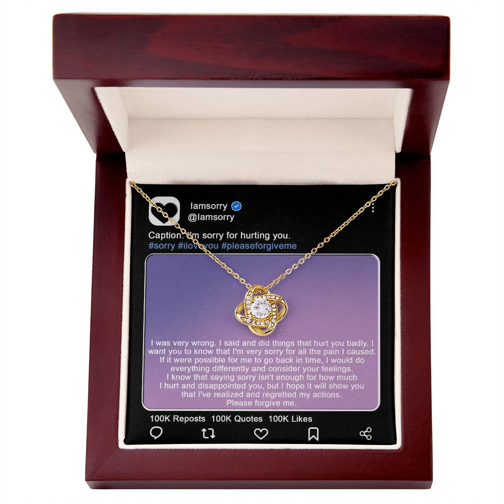 A stunning "Sorry-Hurt You Badly - Love Knot Necklace" in 14k white gold, adorned with cubic zirconia crystals, is displayed in front of a printed Instagram post that includes an apology message and hashtags like #sorry and #iloveyou.