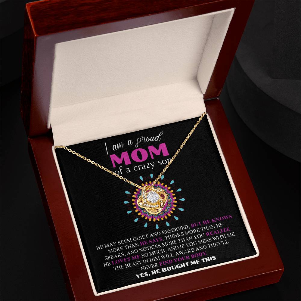 An open jewelry box reveals the "To Mom, Proud Mom - Love Knot Necklace" made of 14k white gold and adorned with dazzling cubic zirconia crystals. The necklace rests on a black insert that bears a printed message about a proud mother of a son.