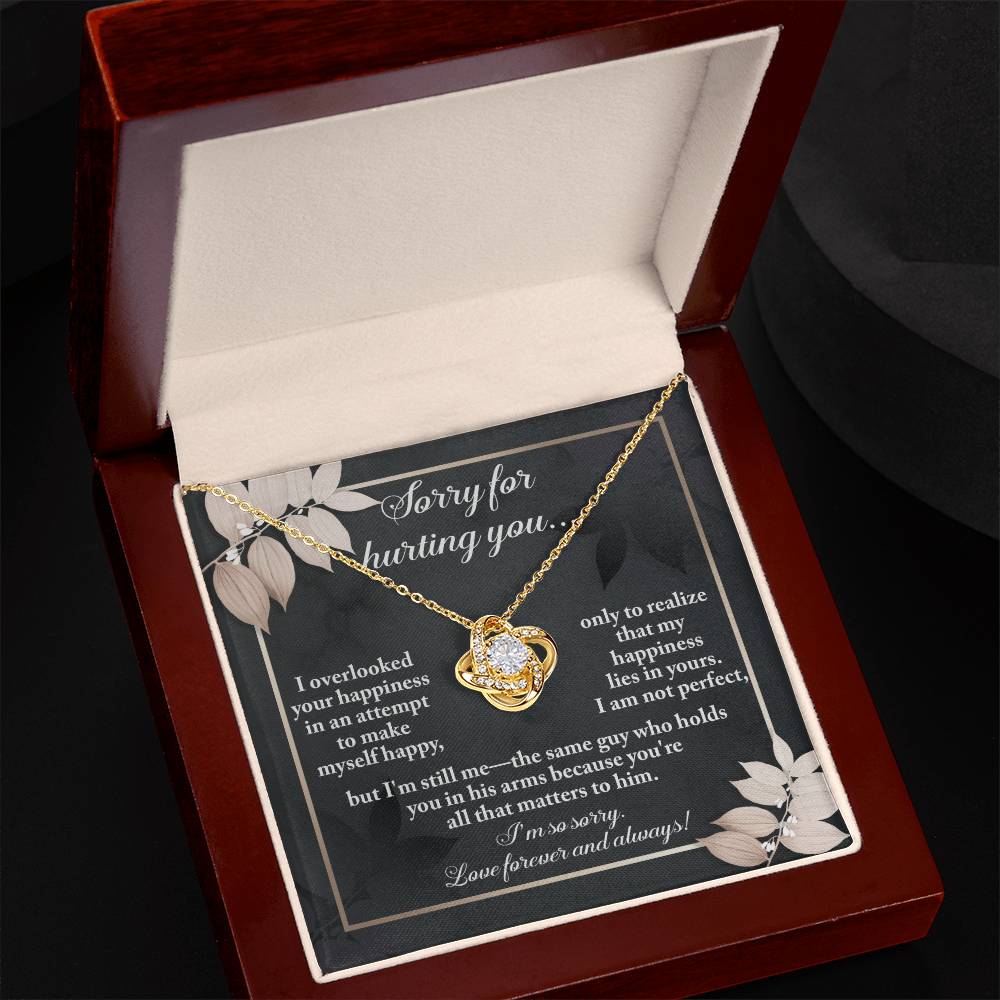 The Sorry-Lies In Yours - Love Knot Necklace, a stunning piece embellished with cubic zirconia crystals, is showcased against a dark-themed backdrop adorned with floral designs. The background beautifully conveys an apology message infused with love and regret.