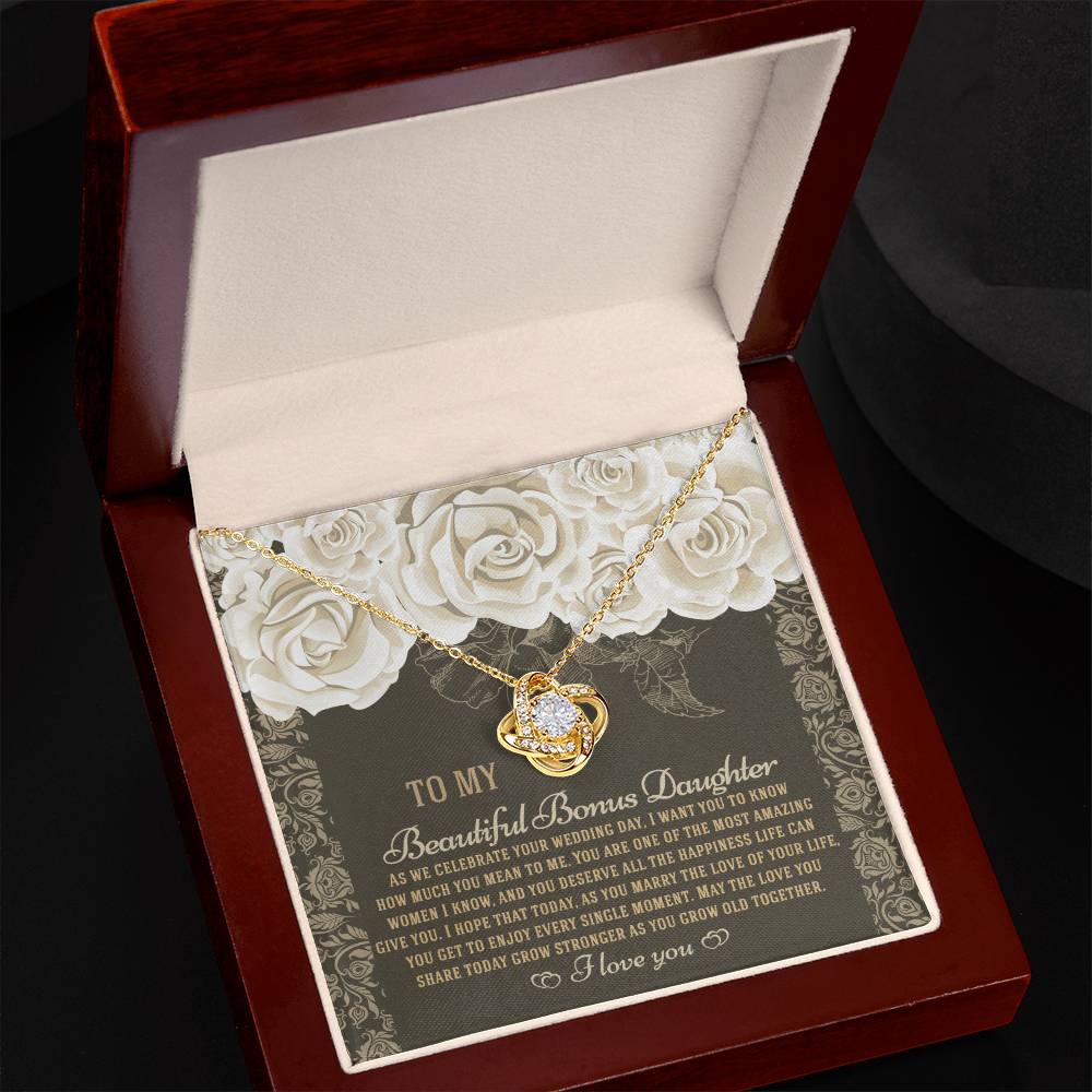 The "To Bonus Daughter, Grow Old Together - Love Knot Necklace" features a gold finish and sparkling cubic zirconia crystals. It comes packaged in a gift box decorated with an ornate floral design and includes a heartfelt message for your daughter on her wedding day.