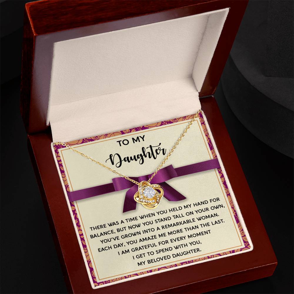 The Daughter-Spend With You - Love Knot Necklace, featuring a heart pendant finished in yellow gold and adorned with cubic zirconia crystals, is displayed in an open box. Inside the box, a message reads, "To my daughter," accompanied by a sentimental note on love and gratitude.