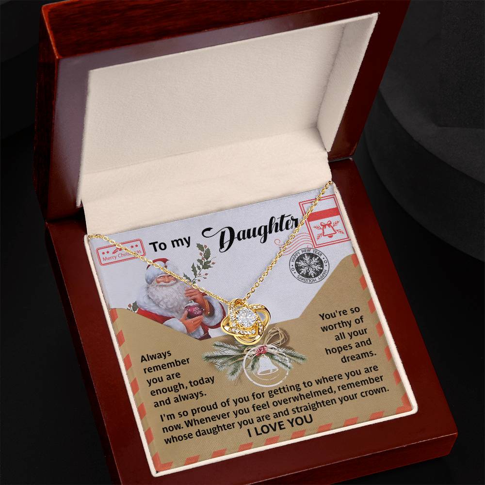 The Daughter-All Your Hopes - Love Knot Necklace, featuring interlocking rings adorned with cubic zirconia crystals and a lustrous gold finish, comes elegantly presented in a jewelry box. It is accompanied by a heartfelt note from a parent to their daughter, complete with festive Santa imagery and sentimental holiday messages that add an extra touch of seasonal magic.