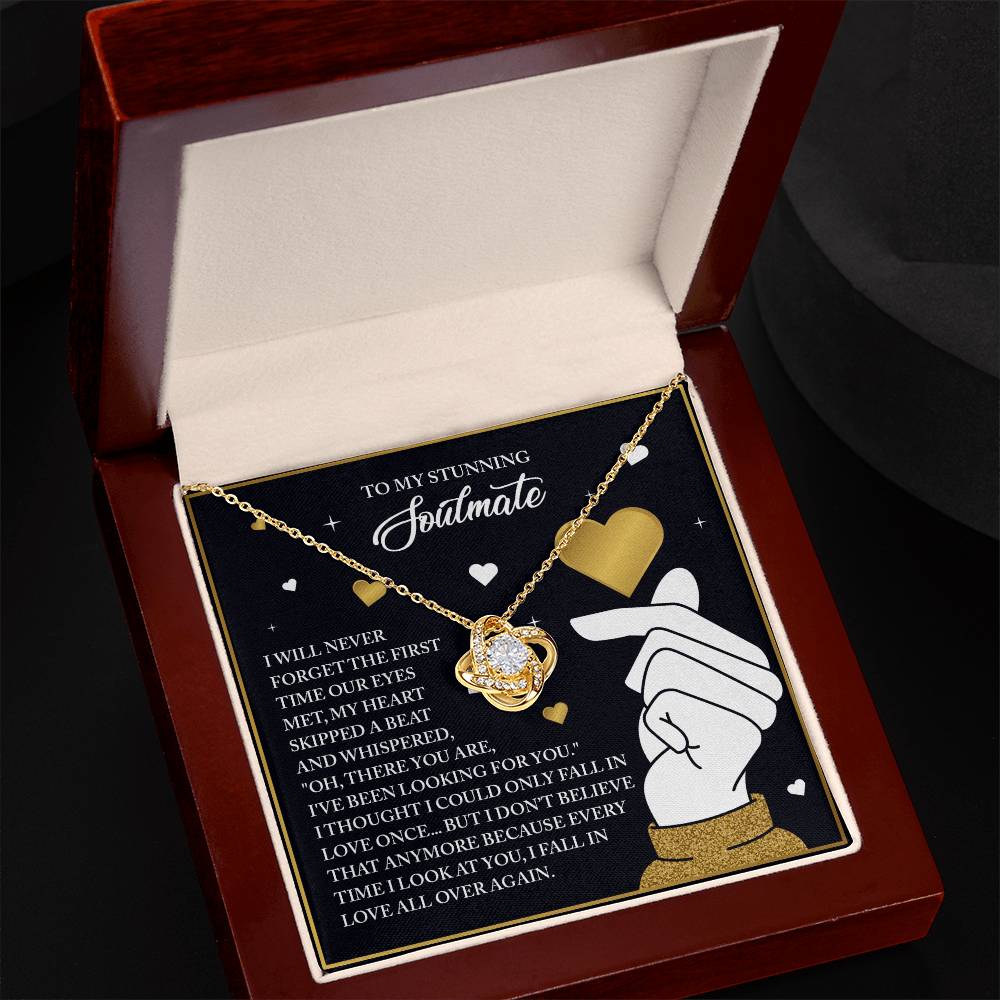 The "Soulmate-Look At You - Love Knot Necklace" features a heart-shaped, gold-finished pendant with cubic zirconia crystals. It comes in a jewelry box with a card displaying romantic text and charming graphics of hearts and hands.