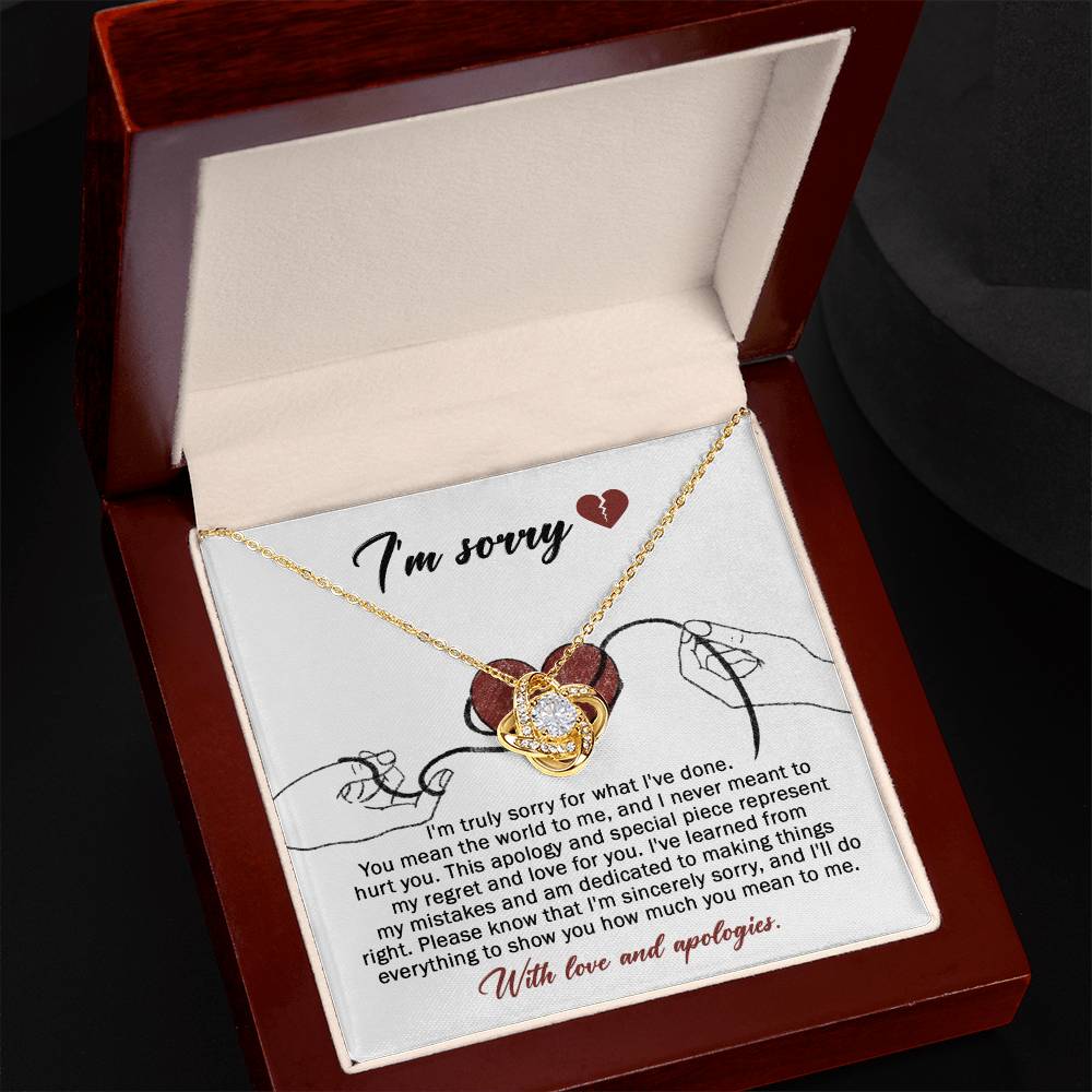 The Sorry-Mean The World - Love Knot Necklace, crafted from white gold and adorned with a heart-shaped pendant, is displayed on a card. This card conveys an apology message expressing regret and dedication to making things right, ending with "With love and apologies." The necklace is embellished with sparkling cubic zirconia crystals that add a touch of elegance.