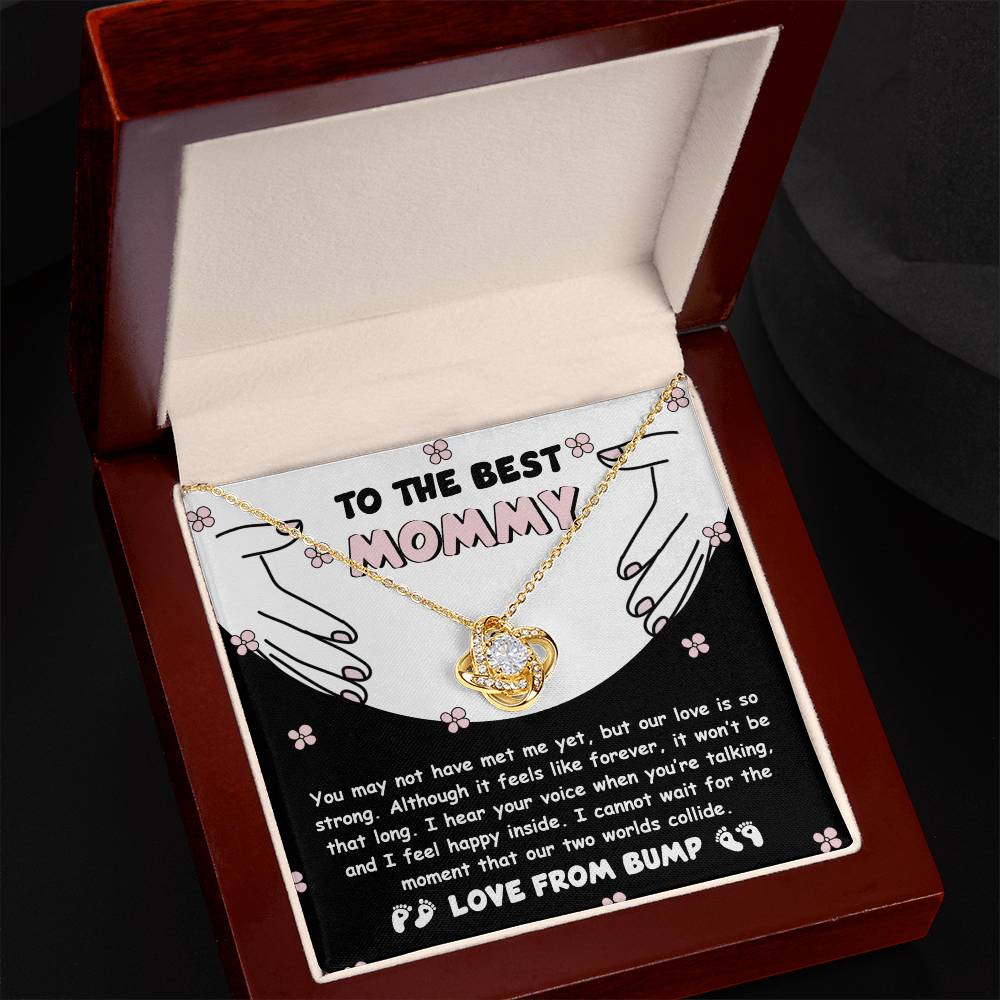 A "To Mom To Be, Two Worlds Collide - Love Knot Necklace" displayed in a box with a heartfelt message addressed to "Mommy" and signed "Love from Bump." The necklace, featuring a heart pendant adorned with cubic zirconia crystals, symbolizes the unbreakable bond between mother and child.