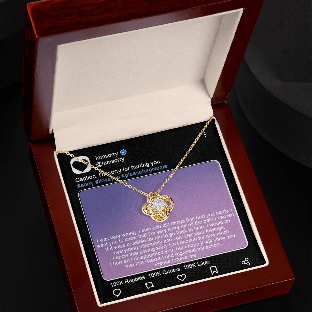 A stunning "Sorry-Hurt You Badly - Love Knot Necklace" in 14k white gold, adorned with cubic zirconia crystals, is displayed in front of a printed Instagram post that includes an apology message and hashtags like #sorry and #iloveyou.