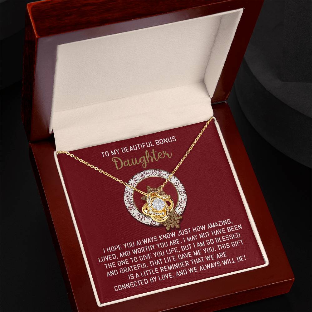 The Bonus Daughter - Always Will Be - Love Knot Necklace features a pendant embellished with brilliant cubic zirconia crystals, presented in an open box. The lid says "To my beautiful bonus daughter," and the base includes a heartfelt message underneath, creating an exceptionally personalized gift.