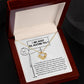 The Sorry-Missing Piece - Love Knot Necklace, adorned with cubic zirconia crystals, sits in an open jewelry box. The box contains a note with an apology message and a stick figure holding a sign that reads, "I am sorry for hurting you.