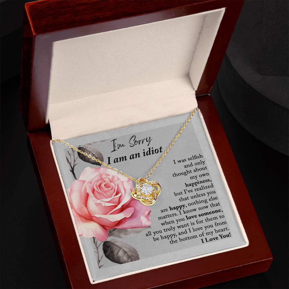 The "Sorry-Love Someone - Love Knot Necklace" is an elegant silver piece with a heart-shaped pendant, adorned with sparkling cubic zirconia crystals. It rests on a beautifully designed box featuring a pink rose and a heartfelt apology note, making it truly a classic gift.