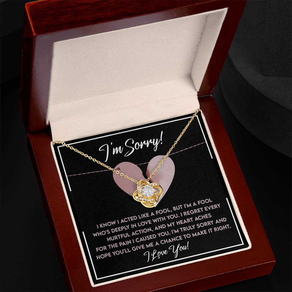 The Sorry-Deeply In Love - Love Knot Necklace, meticulously crafted in 14k white gold and adorned with shimmering cubic zirconia crystals, is elegantly presented in an open wooden jewelry box alongside a heartfelt apology note that reads, "I'm Sorry!" The note conveys remorse for hurtful actions and earnestly seeks forgiveness.