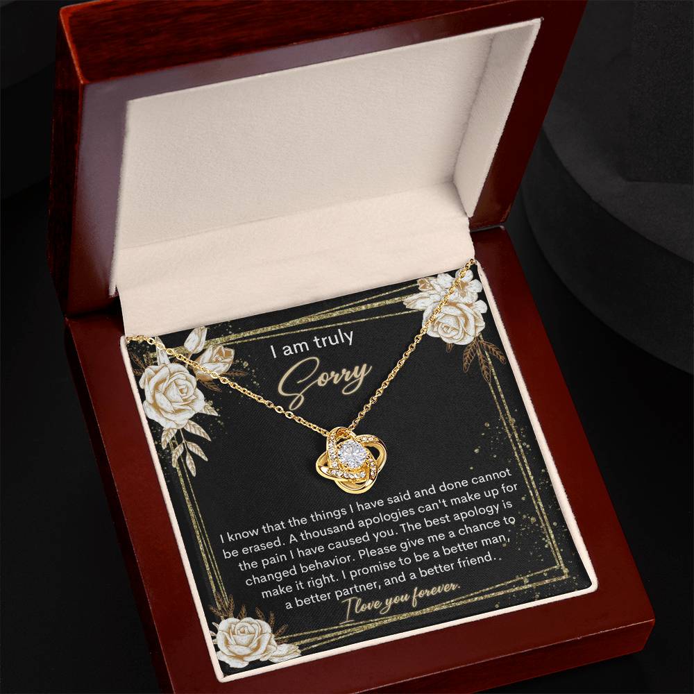 The Sorry-Cannot Be Erased - Love Knot Necklace, adorned with shimmering cubic zirconia crystals and available in a choice of white gold or yellow gold finish, is displayed against a backdrop of a black card bearing an apology message that reads, "I am truly sorry" and "I promise to be a better man, a better partner, and a better friend.