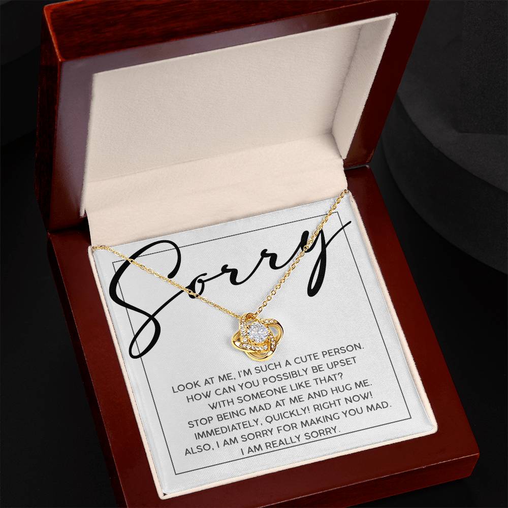 A gold "Sorry-Someone Like That" Love Knot Necklace adorned with cubic zirconia crystals rests in a red box, accompanied by a note saying "Sorry" and an apology message inside.