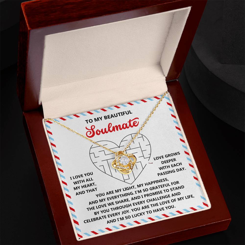 The Soulmate-To Have You Love Knot Necklace, a gold heart-shaped pendant with sparkling cubic zirconia crystals, rests in an open jewelry box with a heartfelt message card—a perfect gift for your loved one.