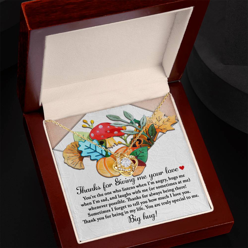 The Thanksgiving-Big Hug Love Knot Necklace showcases a heart pendant with a gold finish, elegantly placed in a box decorated with autumn leaves and an enchanting mushroom illustration, accompanied by a heartfelt note.