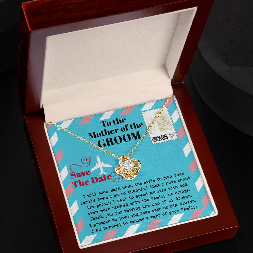 A silver *To Mom Of Groom, Down The Aisle - Love Knot Necklace* with a diamond knot pendant is displayed in a gift box. Adorned with cubic zirconia crystals, the necklace radiates elegance. The box has a message to the "Mother of the Groom" expressing gratitude and a commitment to caring for her son.