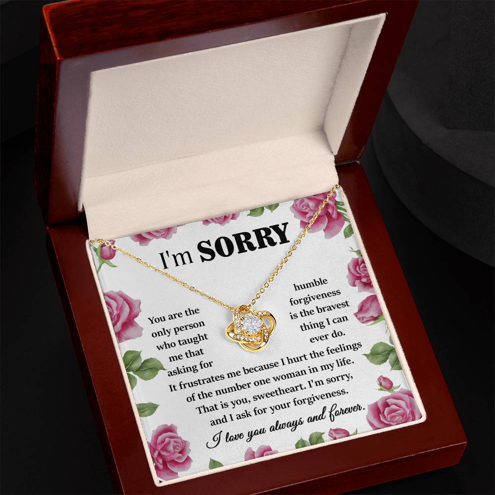 A Sorry-Your Forgiveness - Love Knot Necklace in 14k white gold is placed inside an open gift box, accompanied by a heartfelt apology note adorned with pink roses and sparkling cubic zirconia crystals.