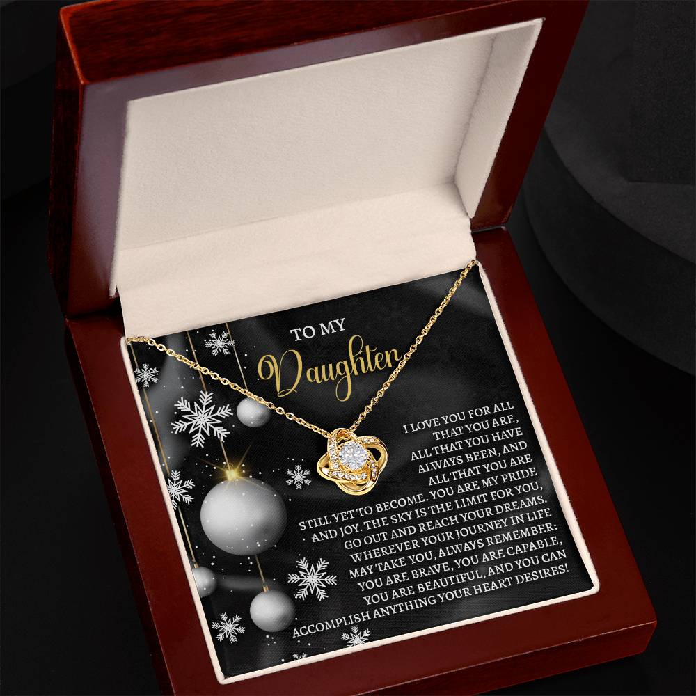 Introducing the Daughter-Pride And Joy - Love Knot Necklace, a stunning gold piece embellished with cubic zirconia, presented in an elegant wooden box. The insert displays a touching message to a daughter, enhanced by snowflake and ornament designs on a black background—making it the perfect personalized gift.