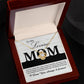 Open the jewelry box containing the "To Mom, Loving As You - Love Knot Necklace," beautifully adorned with sparkling cubic zirconia crystals, and resting on a message card addressed to "My Loving Mom".