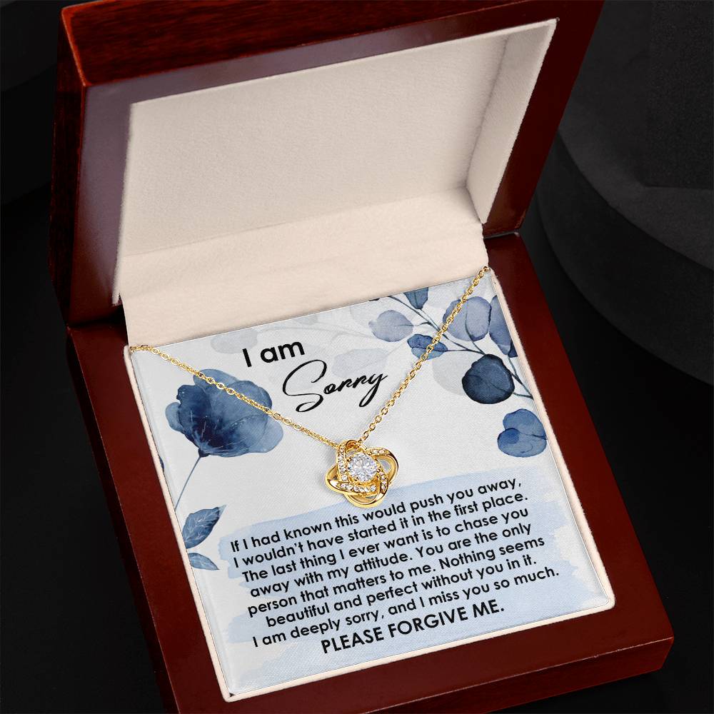 A 14k white gold Sorry-Push You Away - Love Knot Necklace featuring a heart-shaped pendant studded with cubic zirconia crystals is displayed in an open jewelry box. The inside lid contains an apology note with a heartfelt message.