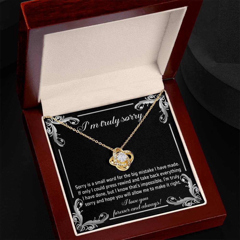 The "Sorry, Make It Right 2 - Love Knot Necklace" showcases a silver interlinked design on a black background. The backdrop features an apology message written in white text, complemented by the brilliance of cubic zirconia crystals.