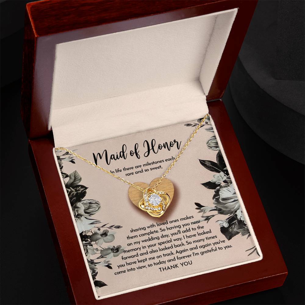 The "To Maid of Honor, My Wedding Day - Love Knot Necklace" features a heart-shaped pendant on a card titled "Maid of Honor," with a heartfelt message about milestones, love, and gratitude. The pendant is available in white gold or yellow gold finish and is adorned with sparkling cubic zirconia crystals.