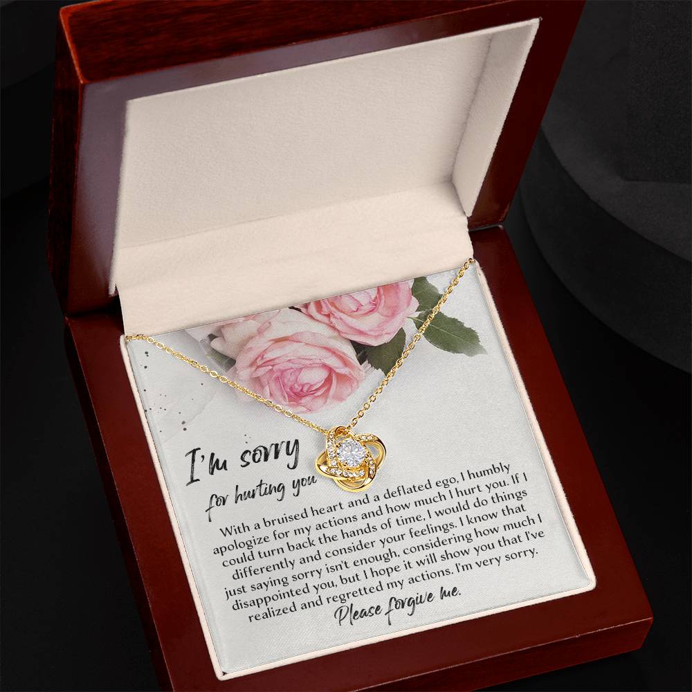 The Sorry-Regretted My Actions - Love Knot Necklace, featuring delicate interlocking hearts and a small gemstone, is elegantly presented in an open, padded jewelry box. The white gold finish enhances its sophistication, while the card inside displays pink roses and an apology message starting with "I'm sorry for hurting you," followed by a heartfelt note.