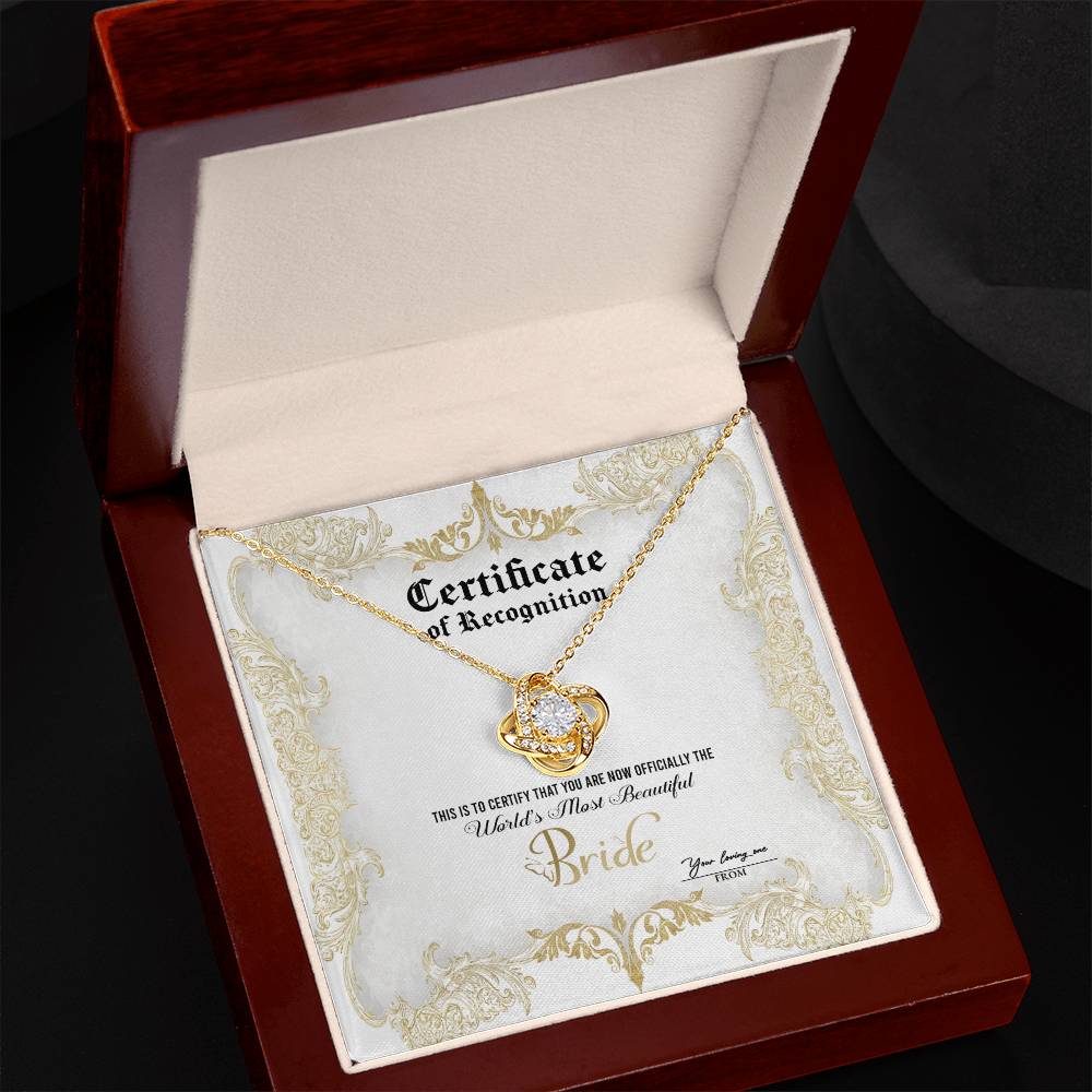 A To Bride, Certificate Of Achievement - Love Knot Necklace with a diamond-studded pendant is inside a box labeled "Certificate of Recognition" with text declaring "World's Most Beautiful Bride" and a space for names "You bring me" and "From." The pendant, set in 14k white gold, sparkles brilliantly.