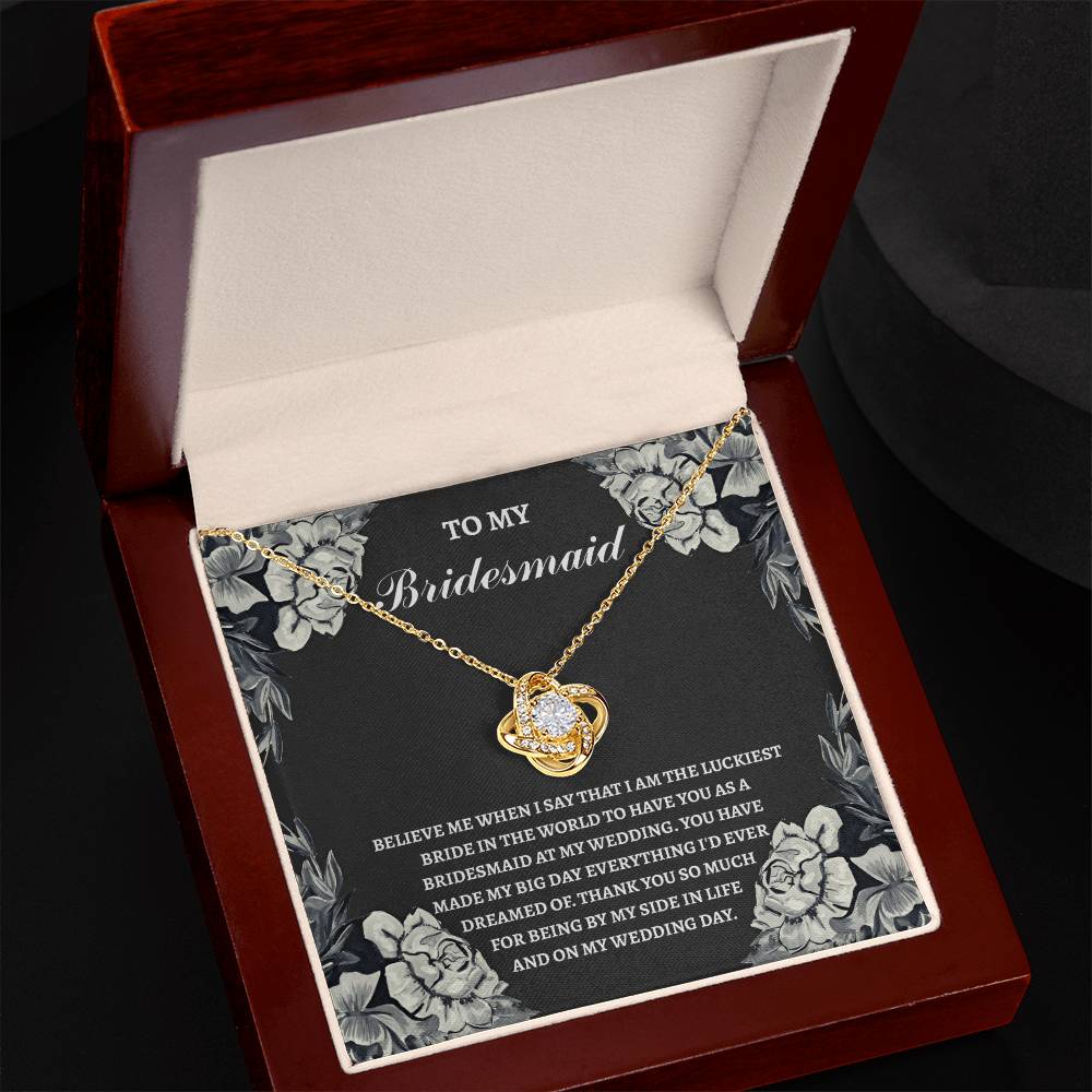 A jewelry box displays the "To Bridesmaid, The Luckiest Bride - Love Knot Necklace" featuring a heart-shaped pendant. The inside lid includes an inscription dedicated to the bridesmaid, making it the perfect Bridesmaid gift.