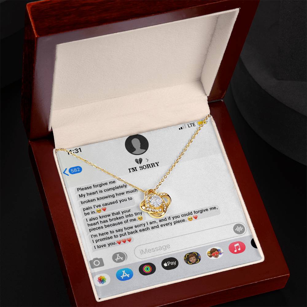 The "Sorry, Completely Broken - Love Knot Necklace" features a gold finish and sparkling cubic zirconia crystals, displayed atop a printed text message conversation that conveys an apology and expresses love.