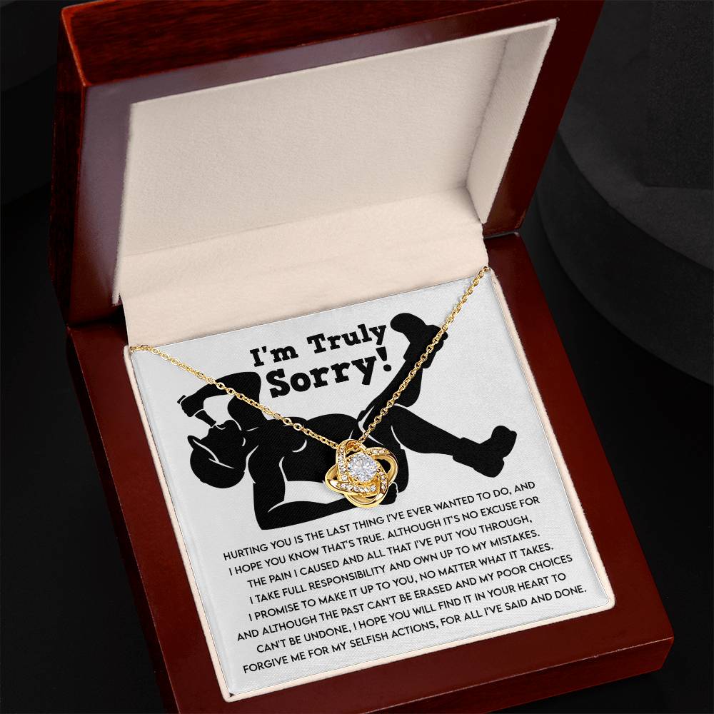 The Sorry-Selfish Actions - Love Knot Necklace with a heart-shaped pendant lies atop a note in an open jewelry box. With its elegant white gold finish and sparkling cubic zirconia crystals, the necklace complements the heartfelt message starting with "I'm Truly Sorry," expressing an apology and seeking forgiveness.