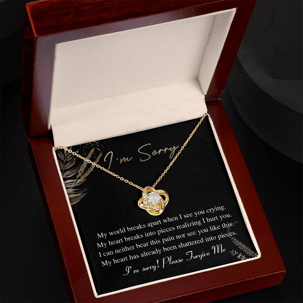 The Sorry-See You Crying - Love Knot Necklace, featuring an intertwined pendant adorned with cubic zirconia crystals, is elegantly displayed on a black card with the inscription "I'm Sorry" and an apology message in white text.