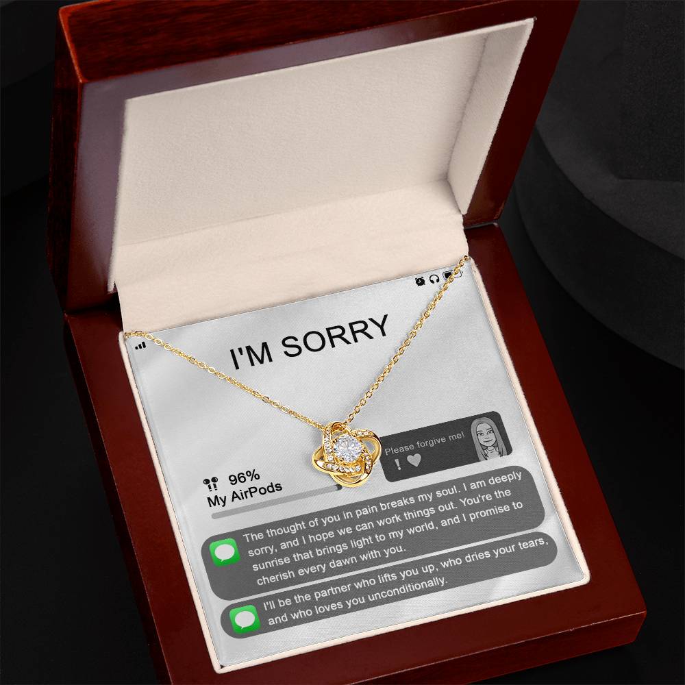 The "Sorry-Breaks My Soul - Love Knot Necklace" is a silver necklace featuring a pendant, beautifully displayed in its packaging. The front of the packaging includes a heartfelt apology message, text messages, a battery icon showing 96% for AirPods, and an illustrated figure. This intricately crafted piece is made from 14k white gold and adorned with cubic zirconia crystals.