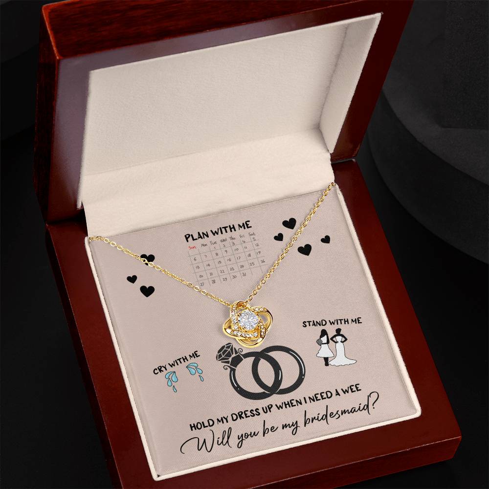 A To Bridesmaid, Will You Be 2 - Love Knot Necklace, adorned with cubic zirconia crystals, is displayed on a card featuring a calendar, wedding rings, and bridesmaid-related illustrations. The text reads, "Will you be my bridesmaid?" Choose from a white gold or yellow gold finish to make the moment even more special.