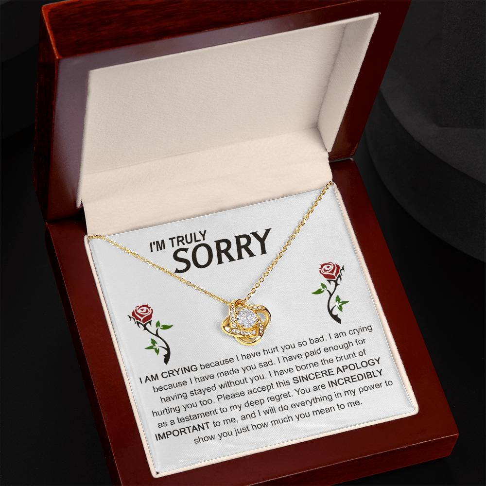 The Sorry-Made You Sad - Love Knot Necklace, crafted in silver with an interlocking design, is presented on a card featuring an apology message and accompanied by two red roses. The text conveys profound regret and vows to make things right, while the cubic zirconia crystals enhance the elegance of this heartfelt gesture.