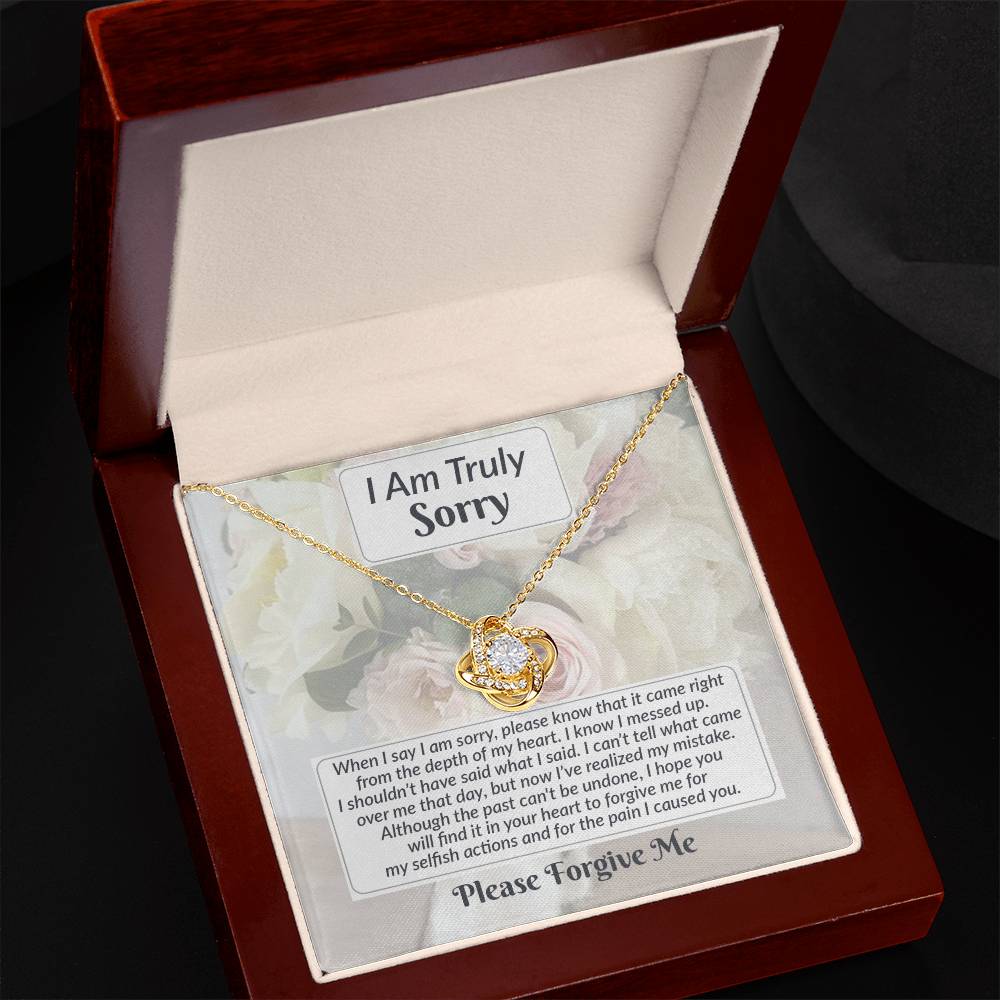 The Sorry-What I Said - Love Knot Necklace features a gold finish chain with a heart pendant adorned with sparkling cubic zirconia crystals, presented inside a wooden box. The box also contains an apology note that says, "I am Truly Sorry," along with a longer message expressing regret and requesting forgiveness.