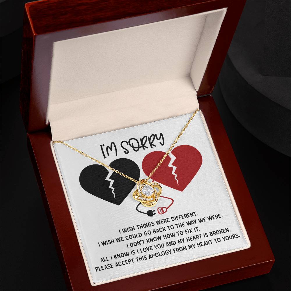 The "Sorry-Heart Is Broken - Love Knot Necklace" features an intertwined heart and infinity design, adorned with cubic zirconia crystals. It is displayed on a card with two broken hearts and a heartfelt message expressing sorrow and hope for reconciliation, all in a stunning white gold finish.