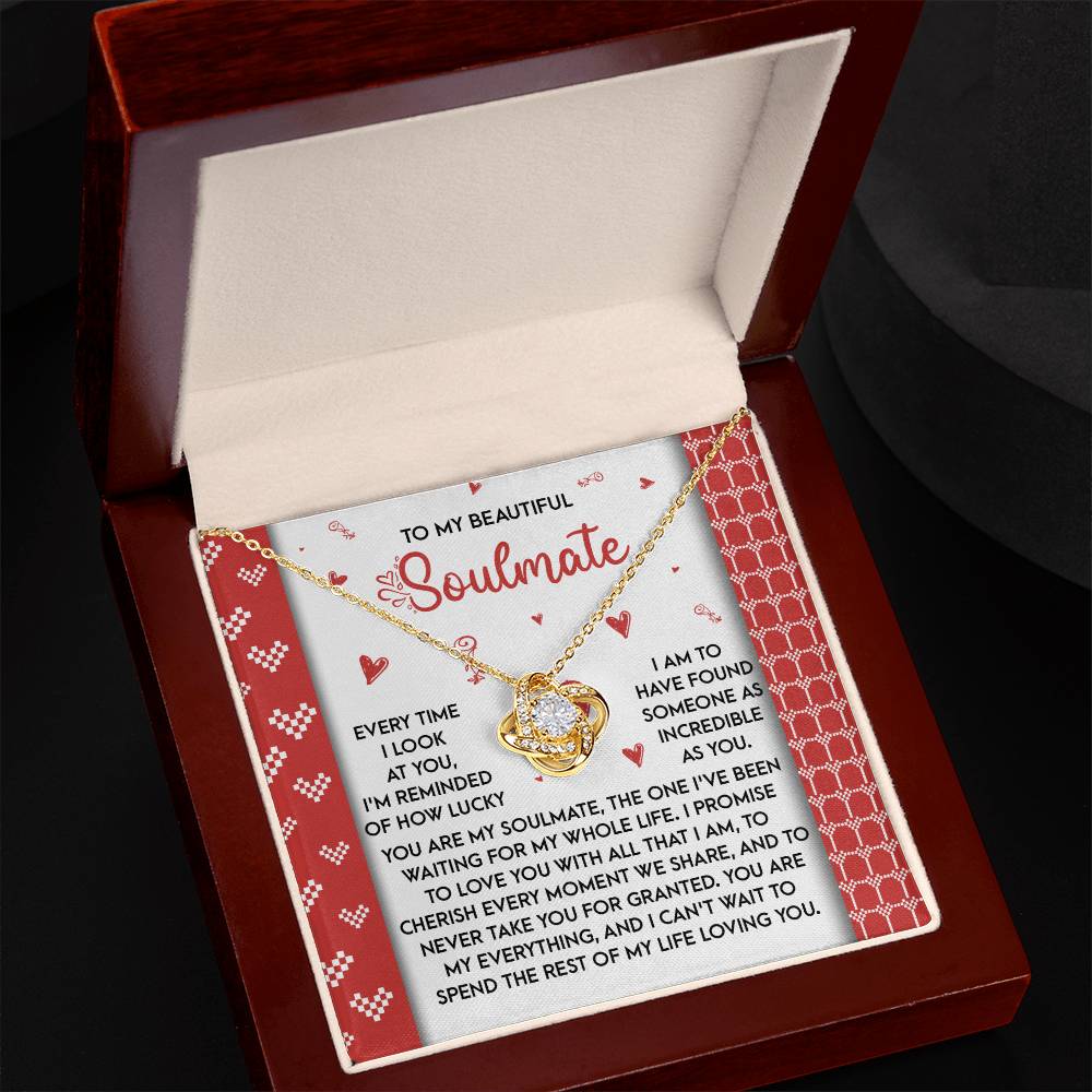 An open jewelry box reveals a stunning Soulmate-My Whole Life - Love Knot Necklace with a gold heart-shaped pendant adorned in cubic zirconia. It rests on a card reading, "To My Beautiful Soulmate," with a heartfelt love message—a truly perfect personalized gift.