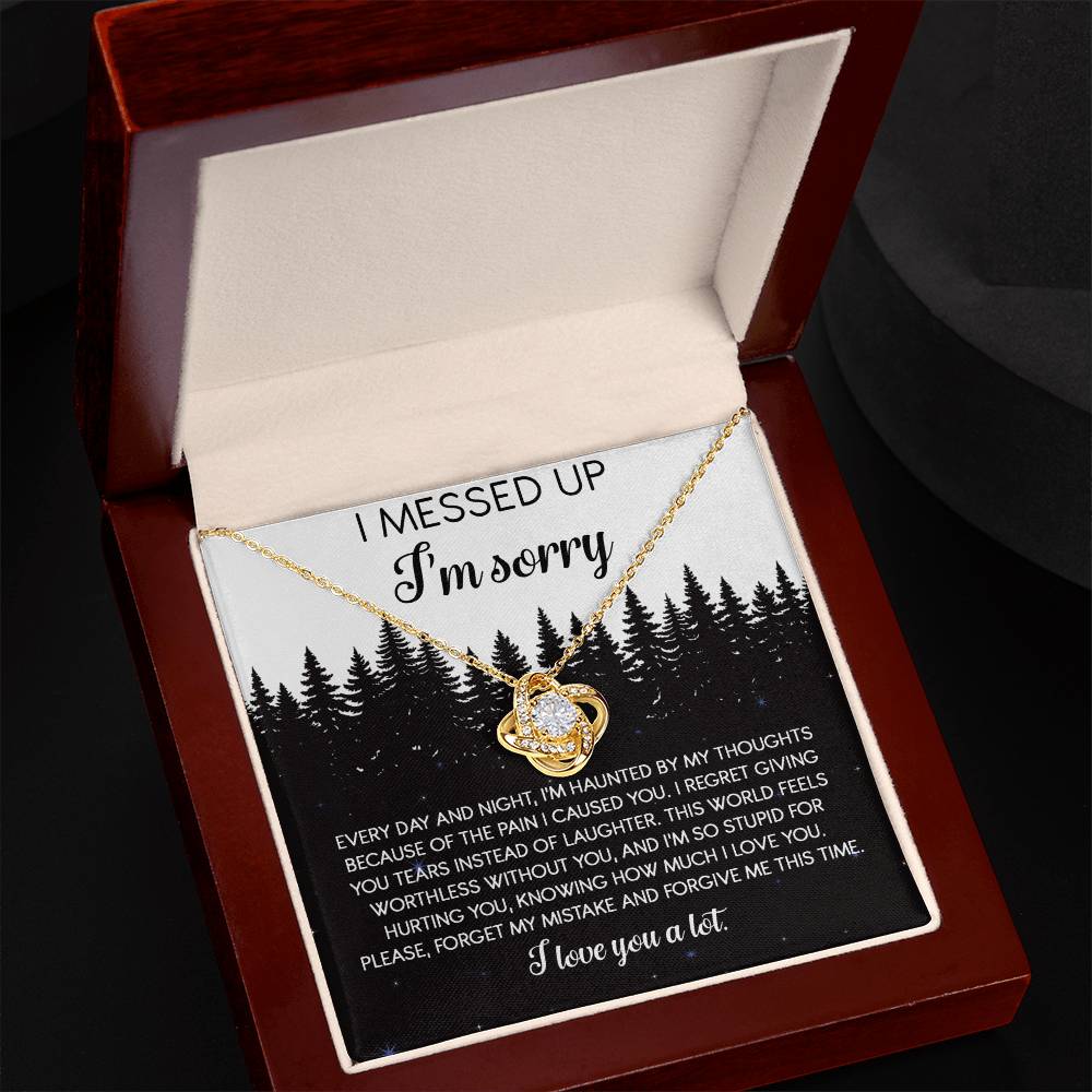 The Sorry-By My Thoughts - Love Knot Necklace, featuring a heart-shaped pendant adorned with cubic zirconia crystals, is displayed on a card with an apology message. The card reads: "I messed up. I'm sorry. Every day and night, I'm haunted...I love you a lot," set against a serene forest background.