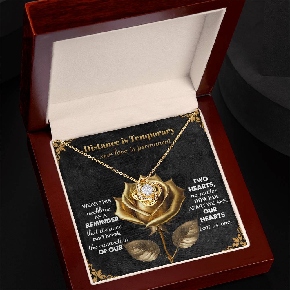 The Soulmate-Love Is Permanent - Love Knot Necklace, embellished with cubic zirconia crystals, showcases an intertwined heart pendant in a jewelry box. A golden rose adorns the backdrop, with text celebrating enduring love—a perfect gift for your special someone.