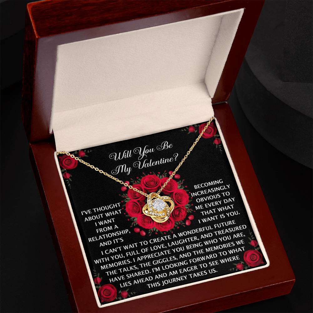 The Soulmate-What I Want - Love Knot Necklace is a gold heart-shaped pendant with a dazzling cubic zirconia, presented in an open box with a romantic message and rose pattern background.