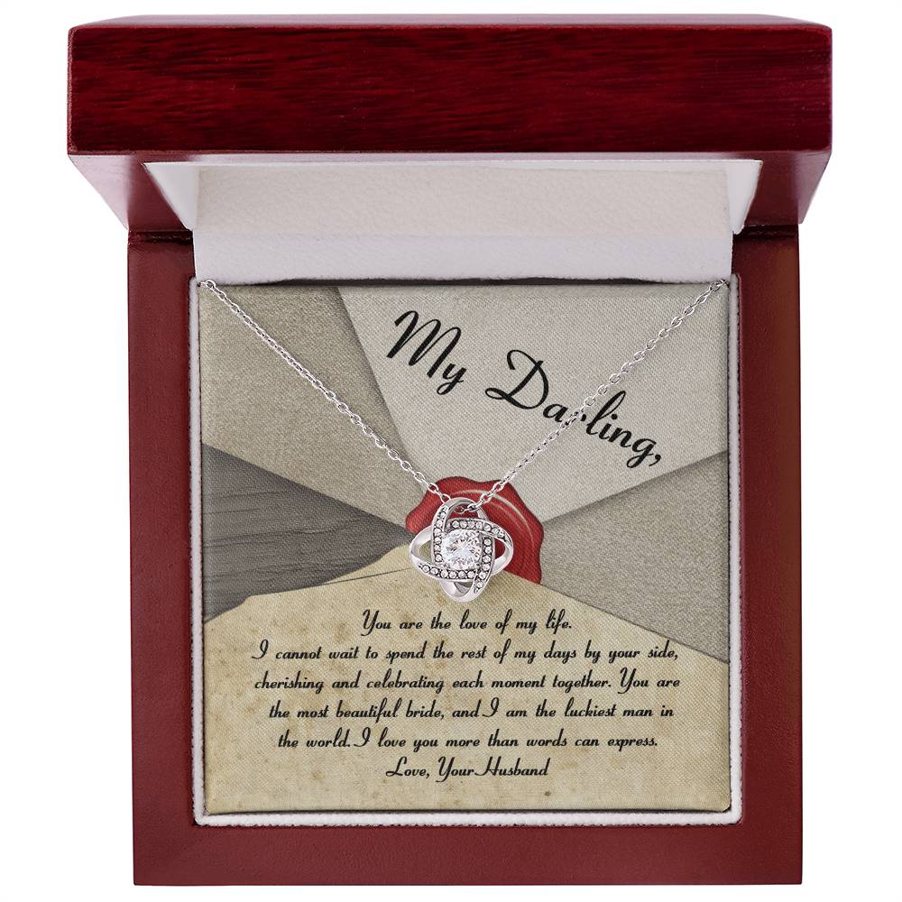 A silver To Bride, Each Moment Together - Love Knot Necklace adorned with cubic zirconia crystals is displayed on a velvet holder, complemented by an overlay message to a bride from her husband, expressing love and commitment.