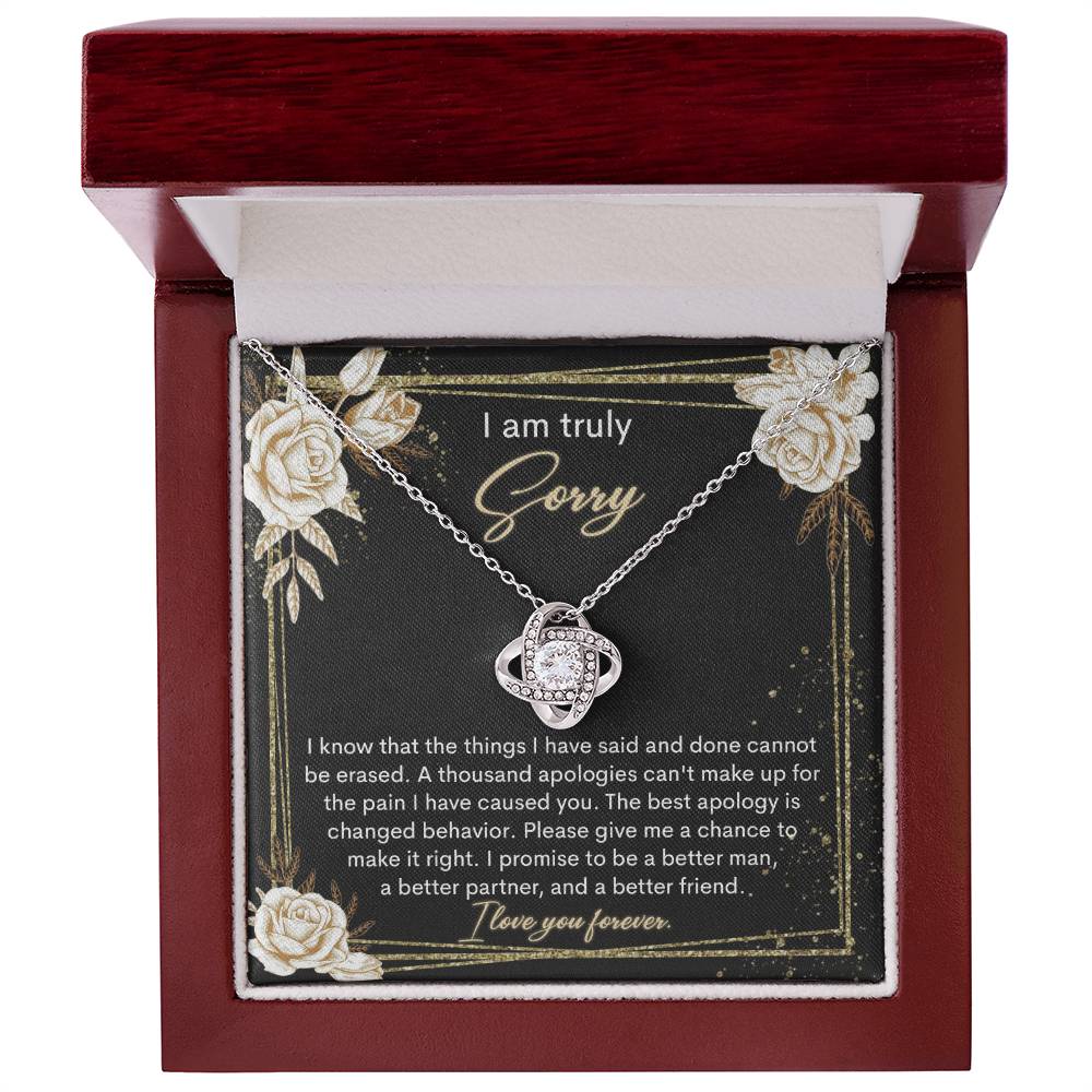 The Sorry-Cannot Be Erased - Love Knot Necklace, adorned with shimmering cubic zirconia crystals and available in a choice of white gold or yellow gold finish, is displayed against a backdrop of a black card bearing an apology message that reads, "I am truly sorry" and "I promise to be a better man, a better partner, and a better friend.